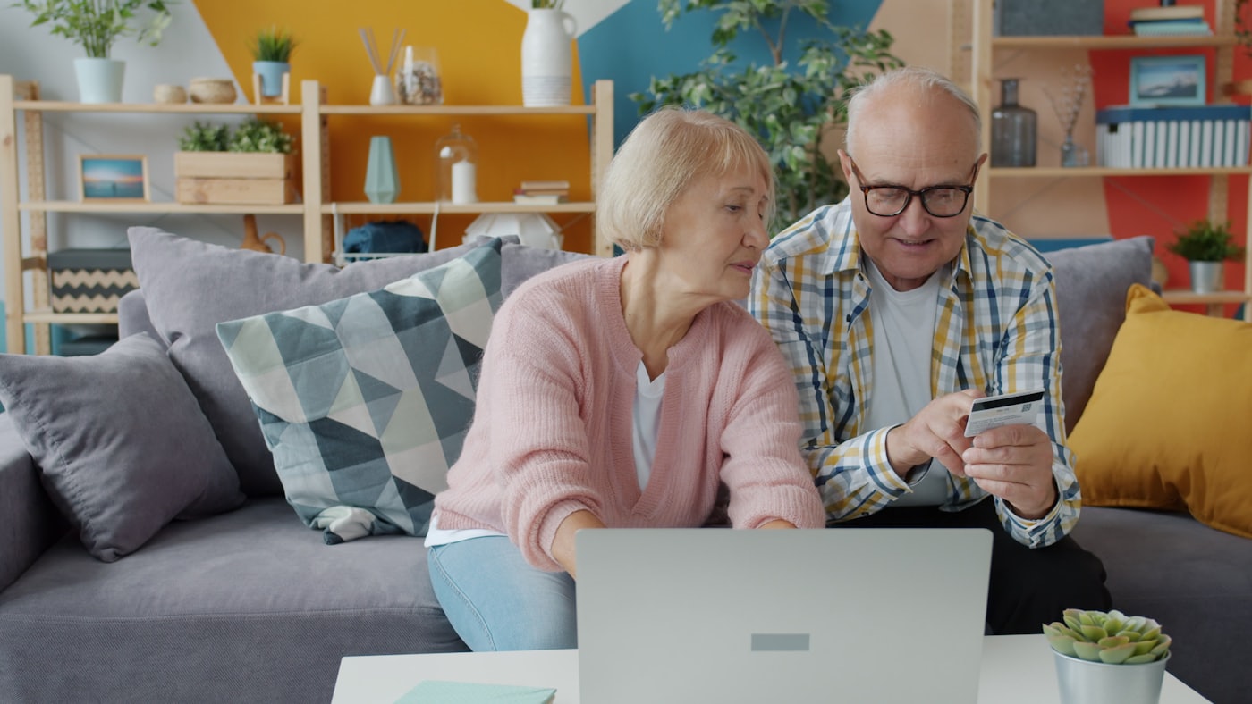 An older couple at a laptop with a credit card in hand.